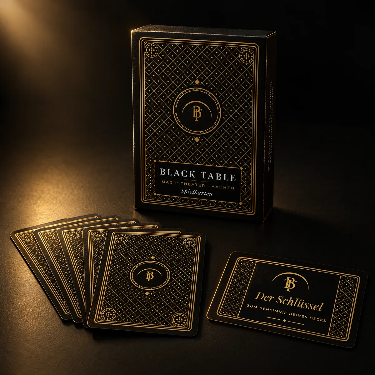 Schwarz-goldene Spielkartenschachtel „Black Table Spielkarten“, davor ein Fächer schwarzer Karten mit Goldmuster und die goldene Schlüsselkarte