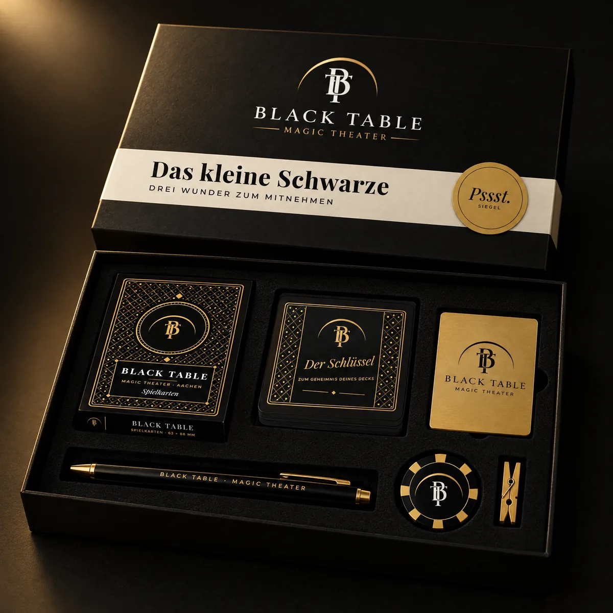 Geöffnete schwarze Magnetbox „Das kleine Schwarze“ mit Goldsiegel, darin Spielkarten, Zahlenkarten, Schlüsselkarte, Kugelschreiber, Casino-Chip und eine goldene Klammer